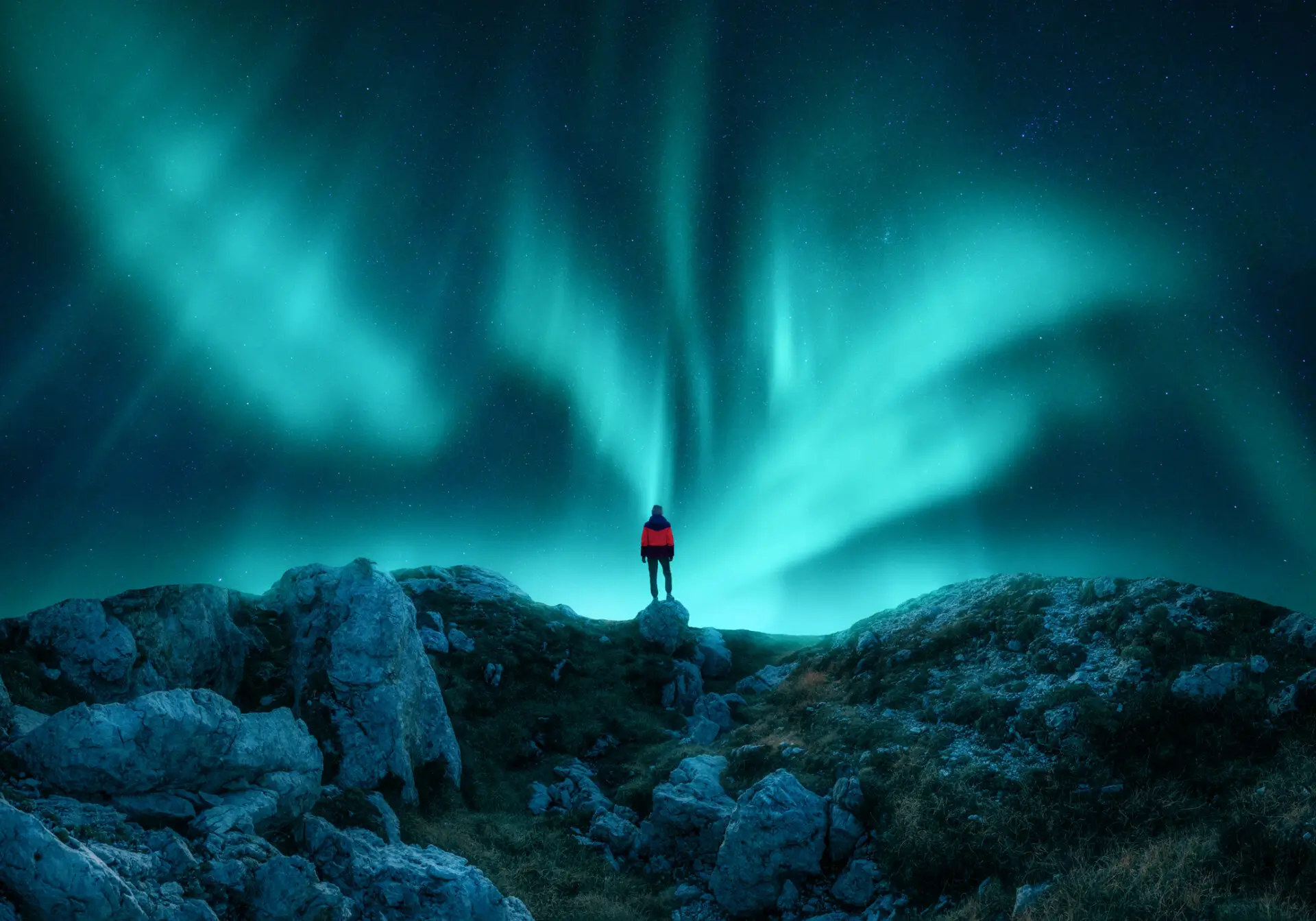 Aurora borealis and young woman on mountain peak at night. Northern lights, stones and silhouette of alone girl on mountain trail. Landscape with polar lights. Starry sky with bright aurora. Travel